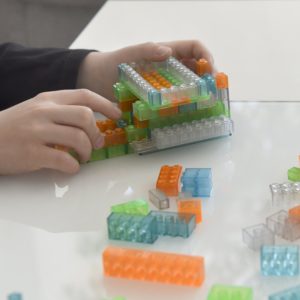 Kinderhände bauen mit transparenten Leuchtspielsteinen in Grün, Blau und Orange