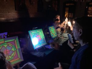 Leuchtende Bilder auf Staffeleien beim Malabend im abgedunkelten Pub