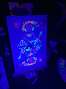 Gemaltes Bild mit Spielkarten-Motiv leuchtet unter Schwarzlicht